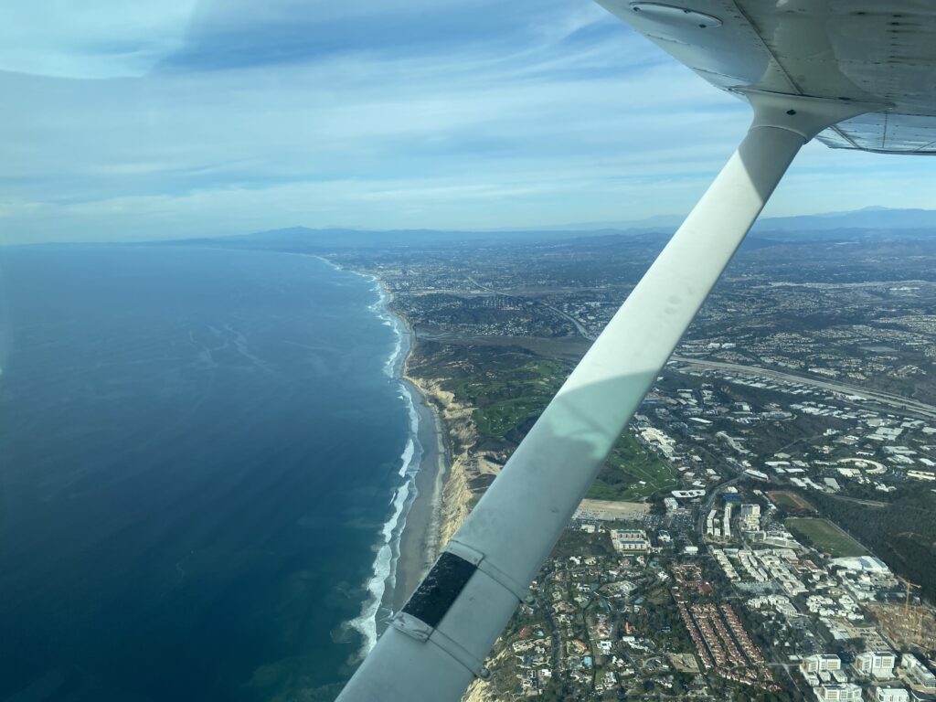 View from inside of a window in an aircraft flying above a city's shoreline